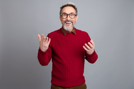 Smiling mature businessman in a red sweater, confidently presenting ideas against a stylish light...