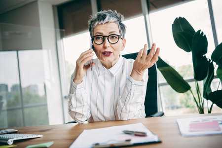 Confident mature businesswoman engaging in a professional conversation in a modern office workspace with bright surroundingsの写真素材