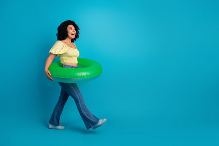 Young woman in vibrant attire holding a green inflatable ring against a blue background, radiating...
