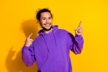 Smiling young man in a purple hoodie making cheerful hand gestures against a bright yellow backgroundの写真素材
