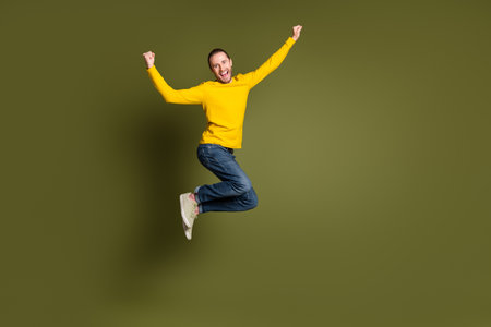 Young Energetic Man in Casual Yellow Sweater Jumping against Green Background
