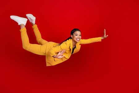Young woman in yellow suit appearing playful and cheerful against a vibrant red backdrop, exuding...