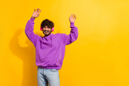 Stylish young man in purple hoodie enjoying music with yellow background, expressing fun and...