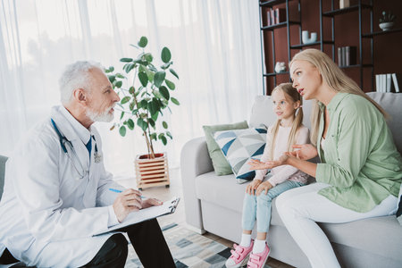 A friendly home visit with doctor talking to mom and daughter about health in a bright living roomの写真素材