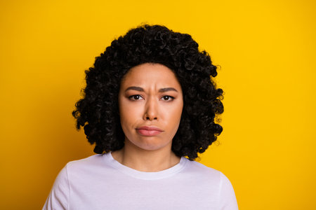Portrait of a Young Woman with Curly Hair Showing a Conflicted Expression Against a Bright Yellow...