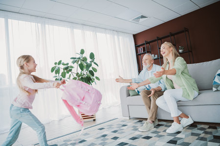 Playful granddaughter rushes to embrace smiling grandparents in a bright living room with a pink...