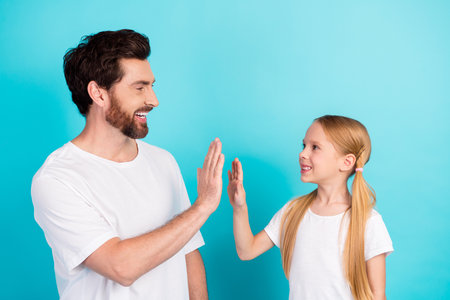 Father and daughter high-fiving against teal background, emphasizing family bonding and cheerful...