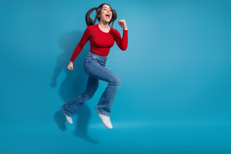 Energetic young woman jumping with joy wearing stylish casual outfit on vibrant blue background