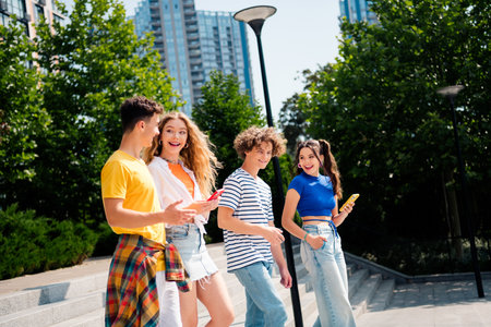 Group of young friends chatting outdoors in a city setting under natural daylight during a sunny summer dayの写真素材