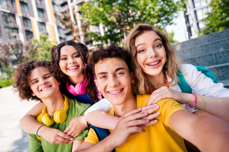A group of cheerful young friends posing together outdoors during a sunny day, embracing and...