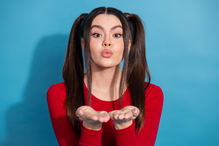 Cheerful young woman in a red casual outfit posing playfully with a kiss expression against a blue backgroundの写真素材