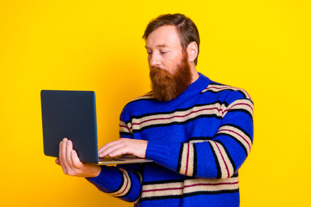 Stylish man with striped sweater using laptop against vibrant yellow background
