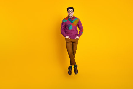 Portrait of a young stylish man in vibrant attire posing against a bright yellow background,...