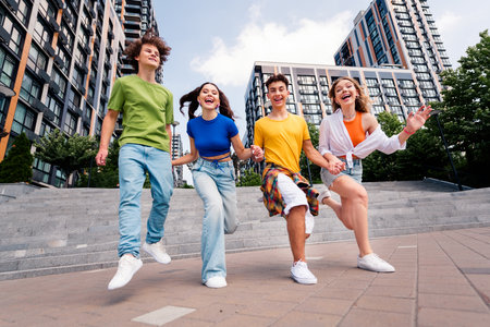 Diverse group of young friends jumping joyfully outdoors in an urban setting, expressing youthful energy and togetherness on a bright dayの写真素材