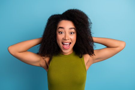 Excited young woman in green top expressing joy with a blue background, embodying happiness and stylish casual fashionの写真素材