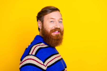 Bearded young man in a vibrant sweater poses confidently against a bright yellow background exuding casual fashionの写真素材