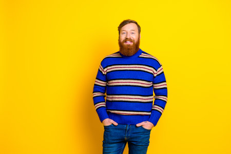 Cheerful young man in a stylish striped sweater posing with confidence against a vibrant yellow backgroundの写真素材