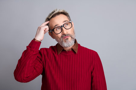 Handsome businessman with glasses pondering an idea against a gray background in a red sweater,...