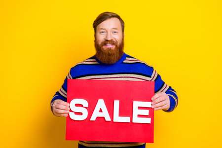 Bearded man holding a red sale sign against a yellow backdrop for a vibrant shopping promotionの写真素材