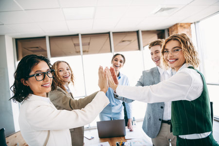 Cheerful office team achieving success together with a high five gesture in a modern professional...