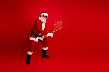 Santa Claus in Holiday Mood Playing Tennis with a Yellow Racket Against a Vibrant Red Backgroundの写真素材