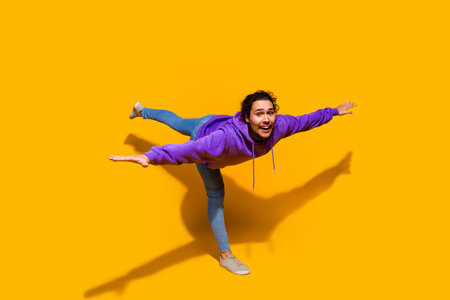 Young man in casual purple hoodie posing playfully against a bright yellow background for fashion...