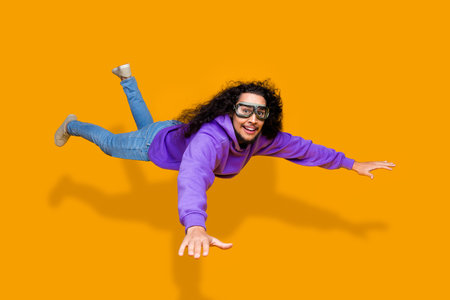 Dynamic young man in purple hoodie and goggles posing against vibrant yellow background exudes energy and styleの写真素材