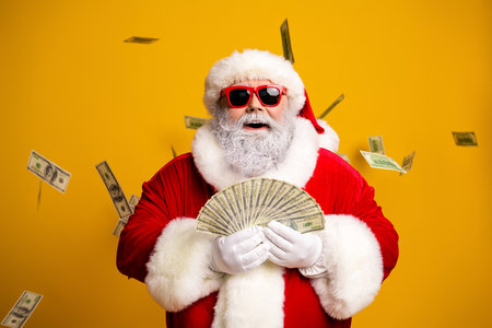 Santa Claus in a stylish outfit surrounded by falling money on a yellow backgroundの写真素材