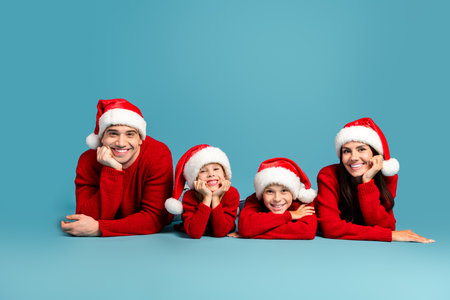Happy family wearing Santa hats and matching red sweaters celebrating Christmas on a blue background, enjoying togethernessの写真素材