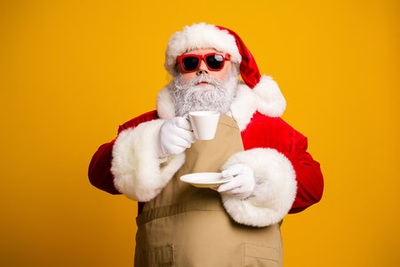 Cheerful Santa Claus in modern style enjoying tea break with vibrant yellow background wearing festive sunglassesの写真素材