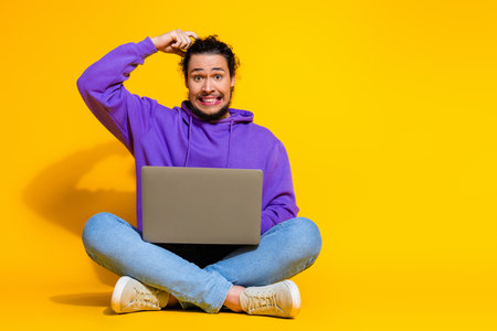 Young man with laptop in a casual style expressing curiosity while sitting on a vibrant yellow...