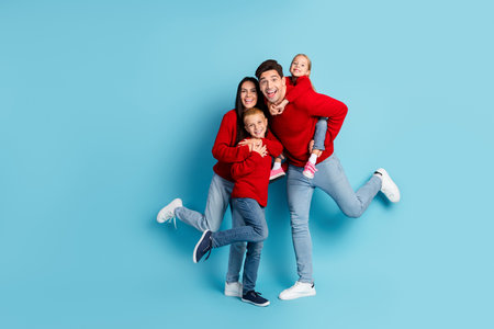 Happy family in festive sweaters jumping joyfully against a blue background celebrating Christmas togetherの写真素材