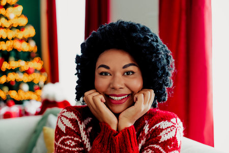 Cheerful woman in festive red sweater enjoying the holiday season in a beautifully decorated room...