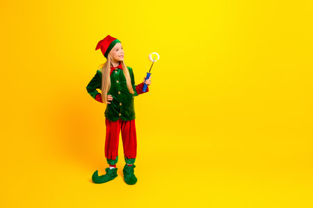 Festive girl dressed in a vibrant elf costume creating a joyful holiday vibe on a yellow background...
