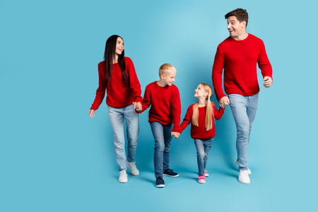 Happy family in red sweaters and jeans enjoying festive moment together against blue background in...