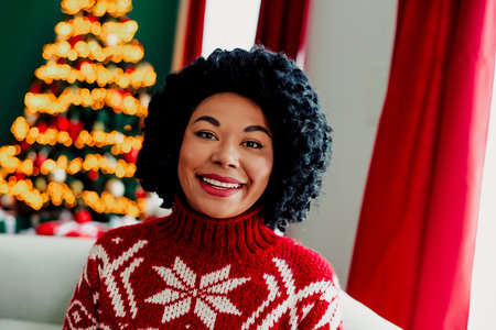 Smiling woman in festive sweater near Christmas tree enjoying cozy holiday atmosphere indoors