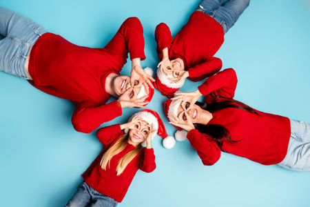 Joyful family in Christmas sweaters creating funny hand gestures on a blue background symbolizing...