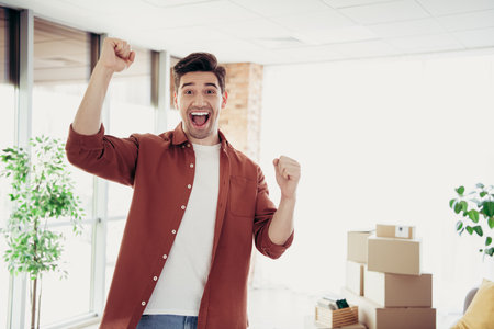 Cheerful man celebrating in a bright living room surrounded by packing boxes, representing a new home and fresh startの写真素材