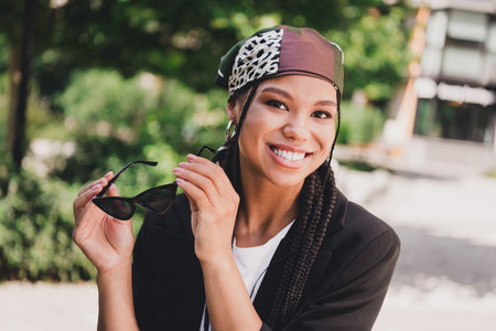 playful street style moment smiling woman with scarf braids wearing blazer and sunglass in sunny...
