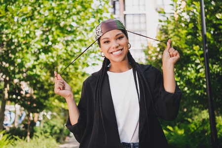 playful modern urban student smiles as she wears a bandana and blazer in the park on a sunny day