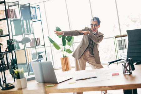 Confident Businesswoman Expressing Joyful Energy in Modern Office Setting with Stylish Attire and Professional Vibeの写真素材