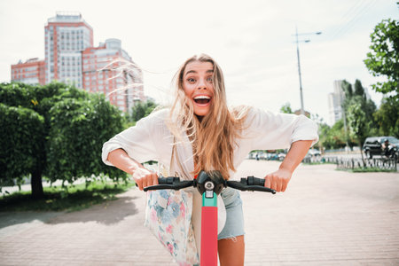 Young woman rides a bright pink scooter through a sunny city street with a joyful smile and carefree modern styleの写真素材