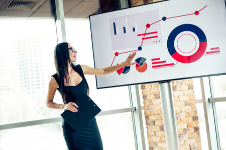 Confident businesswoman presenting financial data and analytics in an office conference with charts and graphs on a screenの写真素材