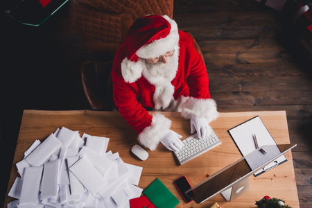 Funny Santa Works Late at Home In a North Pole Workshop Typing at the Desk While Preparing Gifts