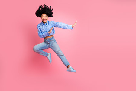 Young woman leaping stylishly on a vibrant pink background expressing joy and energy