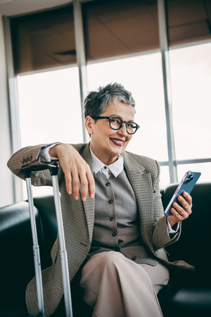 Elegant mature businesswoman at the airport lounge using smartphone while traveling, showcasing...