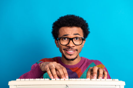 Enthusiastic young man typing on a vintage keyboard with style against a vibrant blue background