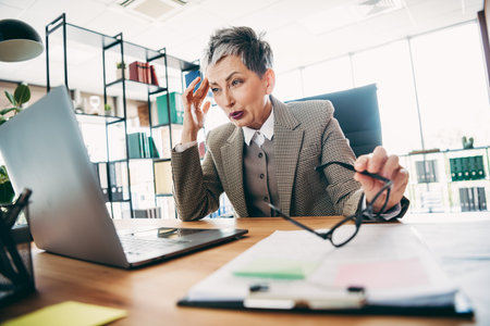 Mature businesswoman working on her laptop in the office expressing emotion during a professional communication processの写真素材