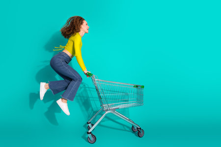 Charming girl woman in casual fashion having fun with shopping cart against a teal backgroundの写真素材