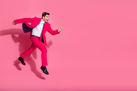 Vibrant young gentleman leaping in stylish pink suit with confident charm on solid pink background showcasing modern trendsの写真素材
